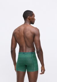 Boxer brev verdi con motivo e una vita elastica che presenta il logo "BJÖRN BORG". Texture liscia e vestibilità contemporanea, mostrati da dietro.