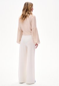 Beige gestreepte blouse met volumineuze mouwen gecombineerd met witte wijde broekspijpen. Gladde stof met een subtiele glans, minimale versieringen.