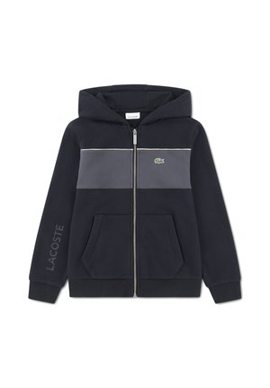 Sweat à capuche zippé bleu marine avec bande grise sur la poitrine, poches avant, capuche, logo Lacoste sur la poitrine et la manche.