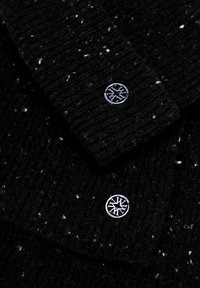 Czarny, prążkowany sweter dzianinowy z białymi kropkami, z dwoma srebrnymi guzikami o okrągłym wzorze na kołnierzu.