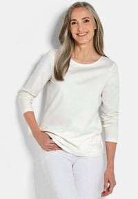 Weißes Langarmoberteil mit Rundhalsausschnitt, glatter Textur und lockerer Passform, kombiniert mit weißen Hosen.