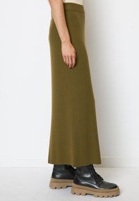 Olijfgroene gebreide maxi rok met een aansluitende taille en een rechte snit, gecombineerd met zwarte leren veterschoenen met stevige zolen.