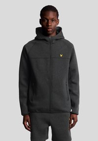 Felpa con zip di colore grigio scuro, dotata di cappuccio e caratterizzata da un piccolo logo giallo sul petto, realizzata in tessuto liscio con due tasche laterali con zip.