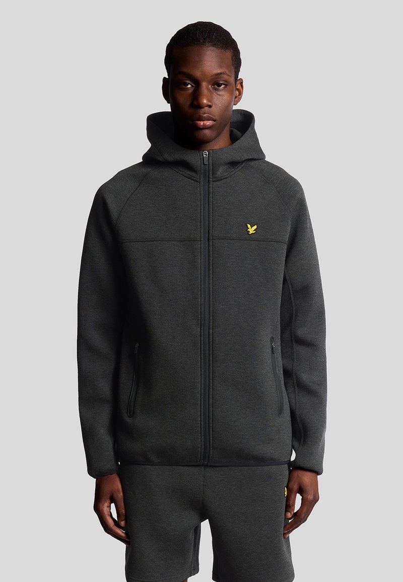 Felpa con zip di colore grigio scuro, dotata di cappuccio e caratterizzata da un piccolo logo giallo sul petto, realizzata in tessuto liscio con due tasche laterali con zip.