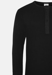 Schwarzes Langarm-Henley-Shirt aus geripptem Baumwollstoff. Mit einem Rundhalsausschnitt und einer Knopfleiste mit drei Knöpfen auf der Vorderseite.