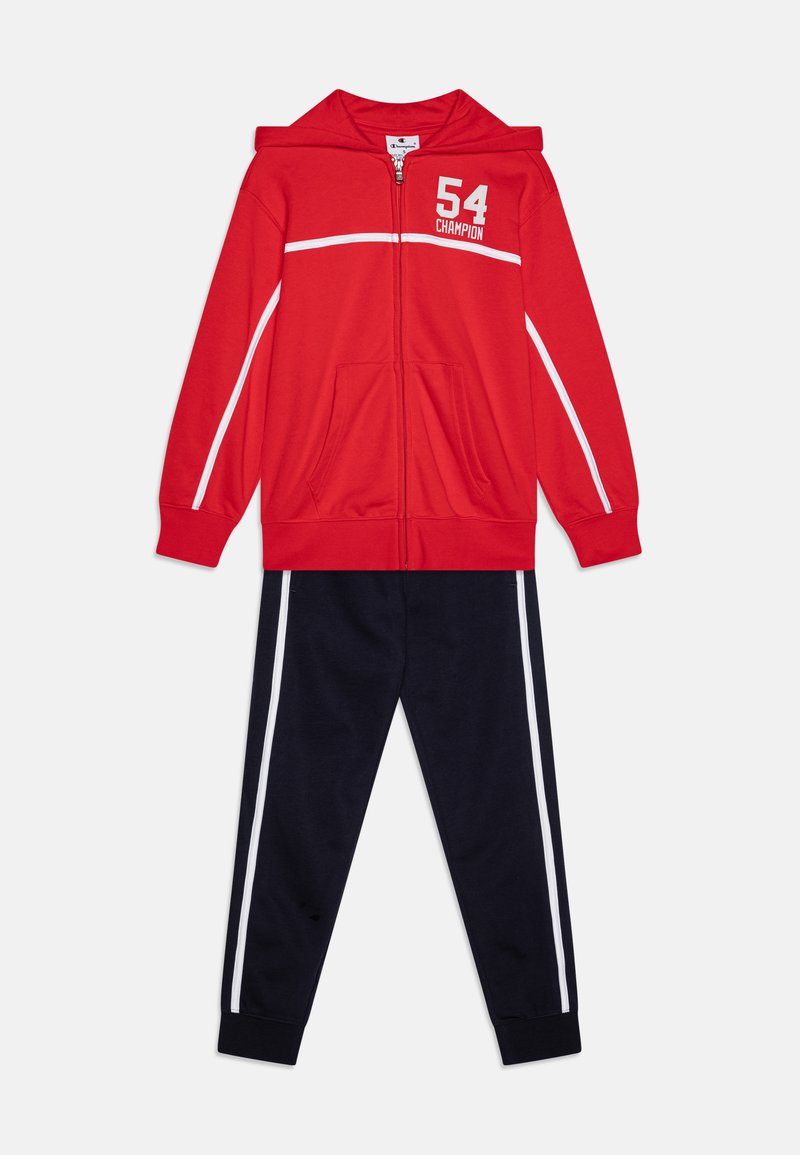 Sarkans ar uzvalciem zip-up hoodijs ar baltām akcentiem un "54 Champion" logotipu, saskaņots ar tumši ziliem biksēm ar baltām sānu svītrām, abi izgatavoti no mīksta auduma.