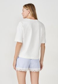Camiseta blanca de algodón con mangas cortas, combinada con pantalones cortos de rayas azul y blanca con un borde de encaje blanco en el dobladillo.