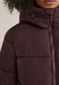 Burgundijas pūkainā jaka ar lielu, izolētu kapuci, priekšējo rāvējslēdzēju un horizontāliem bārkstīm, piedāvājot gludu, matētu apdari.