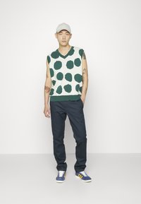 Top verde cu buline albe, fără mâneci, asortat cu pantaloni navy și adidași albaștri cu dungi galbene. Materiale din amestec de bumbac.
