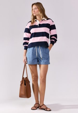 Pullover a righe nei toni del rosa e blu navy, abbinato a pantaloncini di jeans e una borsa marrone. I sandali hanno cinturini sottili. Look casual su uno sfondo chiaro.