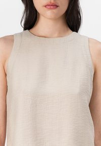 Beiges ärmelloses Oberteil aus strukturiertem Stoff mit rundem Ausschnitt und schlichtem Design. Keine Muster oder Verzierungen.