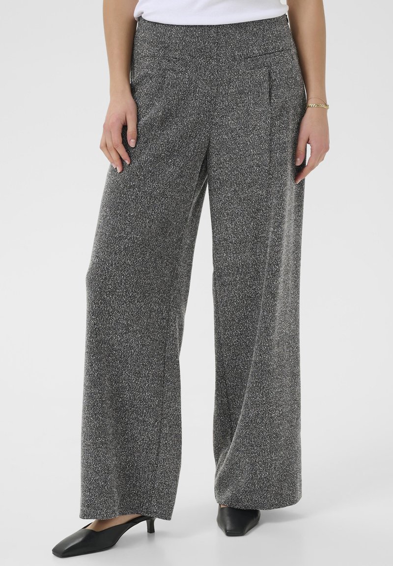 Wijdbenige broek van een zwart-witte gemêleerde brei stof, met voorkeurszakken en een gladde tailleband. Gestyled met zwarte schoenen.
