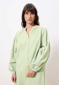 Grün-weiß karierter Button-Up-Kleid mit langen, puffigen Ärmeln und einem Kragenaufschlag. Hergestellt aus leichtem Stoff mit einer weichen Textur.