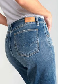 Blauwe denim jeans met een hoge taille, met een leren label aan de achterkant en kenmerkende gebogen stiksels op de zakken.