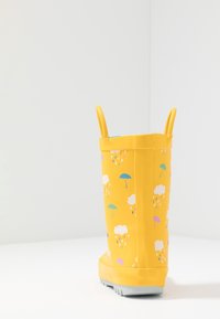 Żółty gumowy kalosz z fakturowaną powierzchnią, zdobiony kolorowymi wzorami parasolek i chmur. Zaprojektowany z dwoma uchwytami ułatwiającymi zakładanie.