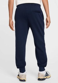 Tumši zili sporta bikses no mīkstas auduma, ar elastīgu jostasvietu, šaurinātām aprocēm un detaļu - kabatu uz muguras. Valkātas kopā ar neitrālām sporta kurpēm.