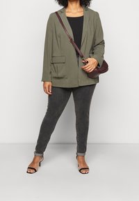 Olivgrön blazer med två framfickor, ihopparad med mörkgrå jeans och svarta öppna klackar. Accenterad med en vinröd axelväska.