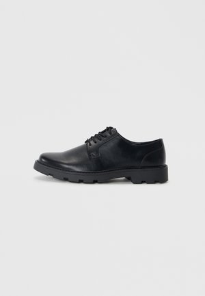 Zapatos de cuero negro con cordones, punta redondeada, suela de goma de perfil bajo y un sutil detalle de costura a lo largo de los bordes.