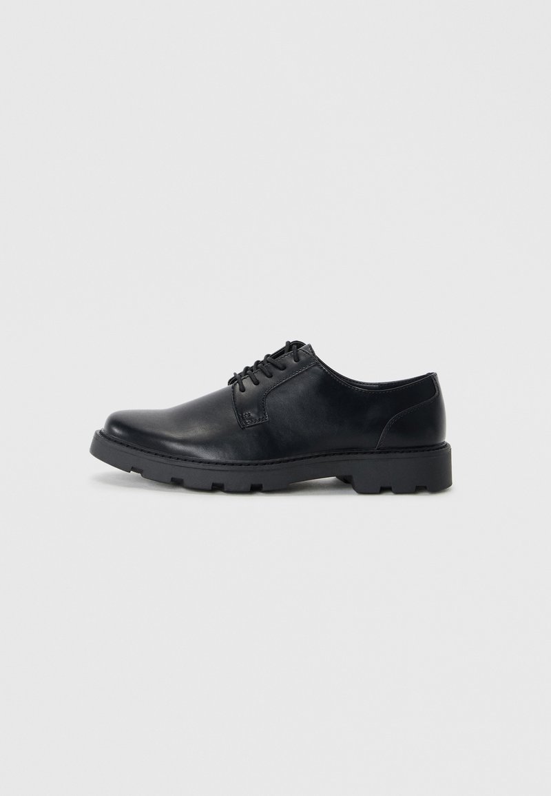 Zapatos de cuero negro con cordones, punta redondeada, suela de goma de perfil bajo y un sutil detalle de costura a lo largo de los bordes.