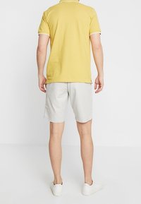Polo da uomo di colore giallo chiaro con rifiniture bianche, abbinato a pantaloni corti grigi chiari. Il tessuto sembra liscio, adatto per un abbigliamento casual.