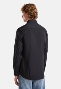 Camicia nera a maniche lunghe realizzata in tessuto liscio, con colletto standard e polsini con bottoni, orlo dritto e retro sagomato.