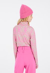 Haut à manches longues de couleur rose clair avec un motif géométrique, associé à un pantalon taille haute rose vif, et un bonnet en tricot texturé rose.
