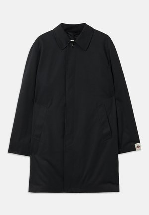 Black coat with a structured collar and button closure, featuring two side pockets and a logo patch on the left sleeve. Smooth fabric texture.