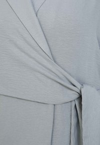 Abito avvolgente grigio chiaro in tessuto testurizzato, con una cintura annodata in vita e pannelli frontali sovrapposti. Materiale morbido e fluido.