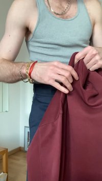 Personne portant un débardeur gris et des bracelets tient un sweat-shirt bordeaux plié à l'intérieur près d'une petite table en bois.