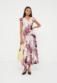 Vestido maxi com estampa abstrata multicolorida, com mangas amplas e decote em V profundo. Combinado com uma mala amarela e saltos pretos.