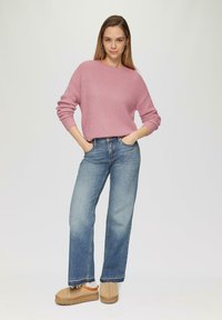 Roze gebreide trui met ribbelstructuur, gecombineerd met lichtblauwe wijde spijkerbroek en beige instappers met tan-zolen.