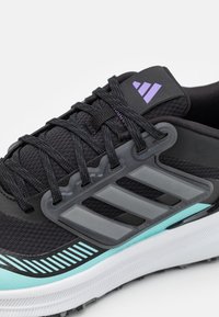 Zwarte sportschoenen met een synthetisch bovenwerk, met grijze accenten, een paarse logo en een gestructureerde mintgroene tussenzool. Veters en gedetailleerde stiksels zichtbaar.