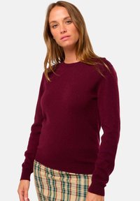 Bordeauxfarbener Wollpullover mit Rundhalsausschnitt und langen Ärmeln, kombiniert mit einem karierten Rock in Creme-, Grün- und Rottönen.