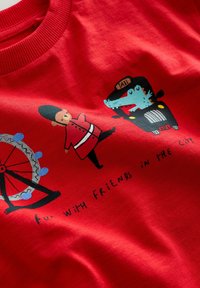 Material roșu cu ilustrații desenate cu un gardian londonez, un taxi condus de un crocodil și o parte dintr-un carusel cu textul „distracție cu prietenii în oraș.”