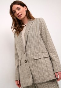 Blazer de cuadros en tonos beige y marrón, con cierre de un botón, dos bolsillos frontales y un corte relajado. Tejido texturizado.