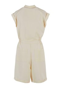 Lys beige jumpsuit med krage, korte ermer, elastisk midje og to baklommer. Glatt stoff med en matt finish.