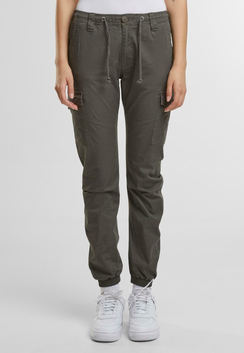 Olive zelené cargo nohavice, vyrobené z ľahkého materiálu, s elastickými manžetami, sťahovacím pásom a dvoma bočnými vreckami. Na nohách sú vidieť biele tenisky.