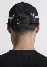 Svart baseballkeps med vit broderi med namnet "Gianagh." Justerbar rem på baksidan; sedd från baksidan.