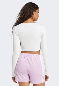 White long-sleeve crop top paired with light pink shorts featuring side snaps and an elastic waistband. Smooth texture, fitted design.