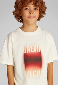 Wit katoenen T-shirt met een verloopontwerp in rood en zwart en grote tekst "CALVIN KLEIN." Korte mouwen en een ontspannen pasvorm.
