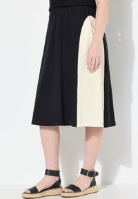 Sort nederdel med et kontrasterende cremefarvet panel, elastisk talje og en afslappet A-formet silhuet. Sammen med sorte espadrille-sandaler.