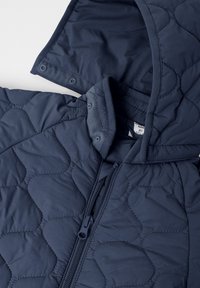 Marineblå quiltet jakke med hætte, som har lynlåslukning, trykknapper og et struktureret mønster på stoffet.
