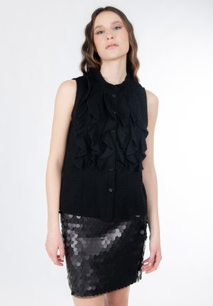 Zwarte mouwloze top met ruches aan de voorkant en knoopsluiting, gecombineerd met een glanzende zwarte paillettenrok met cirkelvormige schijfjespatronen.