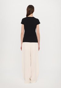 Schwarz, kurzärmliges T-Shirt mit rundem Ausschnitt, kombiniert mit weiten beigen Hosen. Der Stoff wirkt weich und glatt, mit einer taillierten Silhouette.