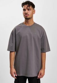 Grå oversized t-shirt lavet af bomuld. Korte ærmer, rund hals, og lille logo-detail på brystet. Enkel og glat tekstur.