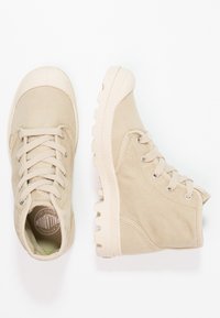Béžové kotníkové plátěné tenisky s gumovou špičkou a texturovanou podrážkou. Obsahují kulaté tkaničky a kovové okénka pro bezpečné zavazování.