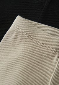 Tissu côtelé montrant deux sections : une section noire et une section beige, chacune ayant des détails de couture visibles le long des bords.