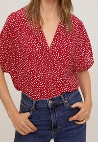 Rode korte mouwen shirt met witte stippen, knopen aan de voorkant en een V-hals ontwerp, gecombineerd met donkerblauwe hoge taille jeans.