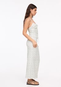 Rochie maxi cu imprimeu floral, cu bretele subțiri, design plisat, din material ușor, în nuanță crem cu flori albastre și verzi; asortată cu sandale plate.