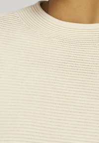 Helle beige gestrickte Sweater mit einer gerippten Textur und Rundhalsausschnitt, ausgestattet mit horizontalen Streifen und einem weichen Finish.